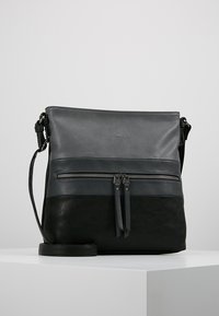 Bolso de cuero cruzado en gris y negro. Cuenta con un bolsillo frontal con cremallera, dos anillas para la cremallera y una correa ajustable. Acabados lisos y texturizados.