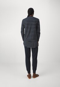 Långärmad topp i marinblått och vitt randig, kombinerad med marinblå byxor. Mjuk bomullsmaterial, avslappnad passform och smalnade manschetter på byxorna.