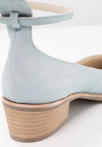 Chaussure à bride cheville en daim bleu clair avec un bout rond et un talon en bois empilé, présentant une texture lisse et des détails de couture minimalistes.