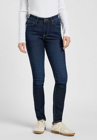 Mörkblå denimjeans med hög midja, smal passform och guldtrådsstickning. Har en framknapp och dragkedjestängning, med standard femfickorsdesign.
