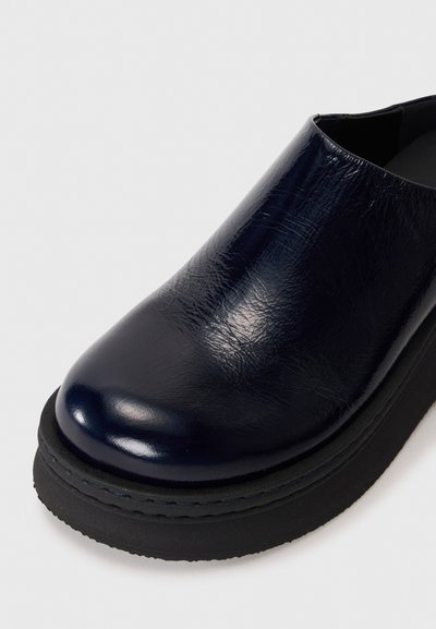 Chaussure en cuir verni bleu marine sombre avec un orteil arrondi et une semelle en caoutchouc noir épais, vue en gros plan de face.