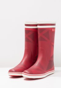 Bottes de pluie en caoutchouc rouge avec motif géométrique et accents blancs, dotées d'un dessus flexible et d'une semelle texturée pour une meilleure adhérence.