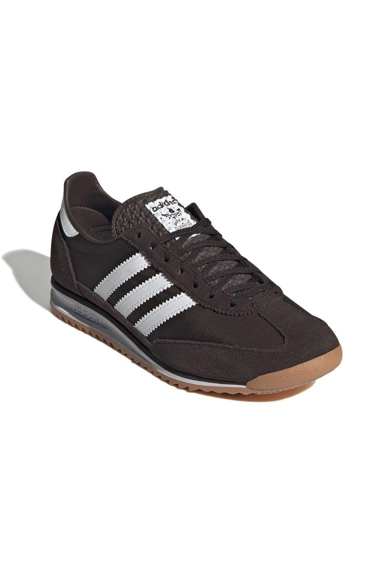 Chaussure de sport noire avec un matériau en suède et en maille. Présente trois bandes blanches, une languette texturée et une semelle en gomme.