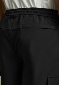 Sorte cargo-bukser med elastisk talje, glat tekstur og en sidelomme. Har minimalistisk design og strømlinet silhuet.
