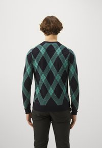 Marinblå tröja med ett geometriskt teal argyle-mönster, ribbade ärmslut och nederkant; medelhavstjocklek, blandning av bomullsmaterial, långa ärmar.