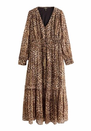 Kvinde med løst hår iført en lang, brun leopardprint kjole med knapper og sorte ankelstøvler, stående på mørkt trægulv.