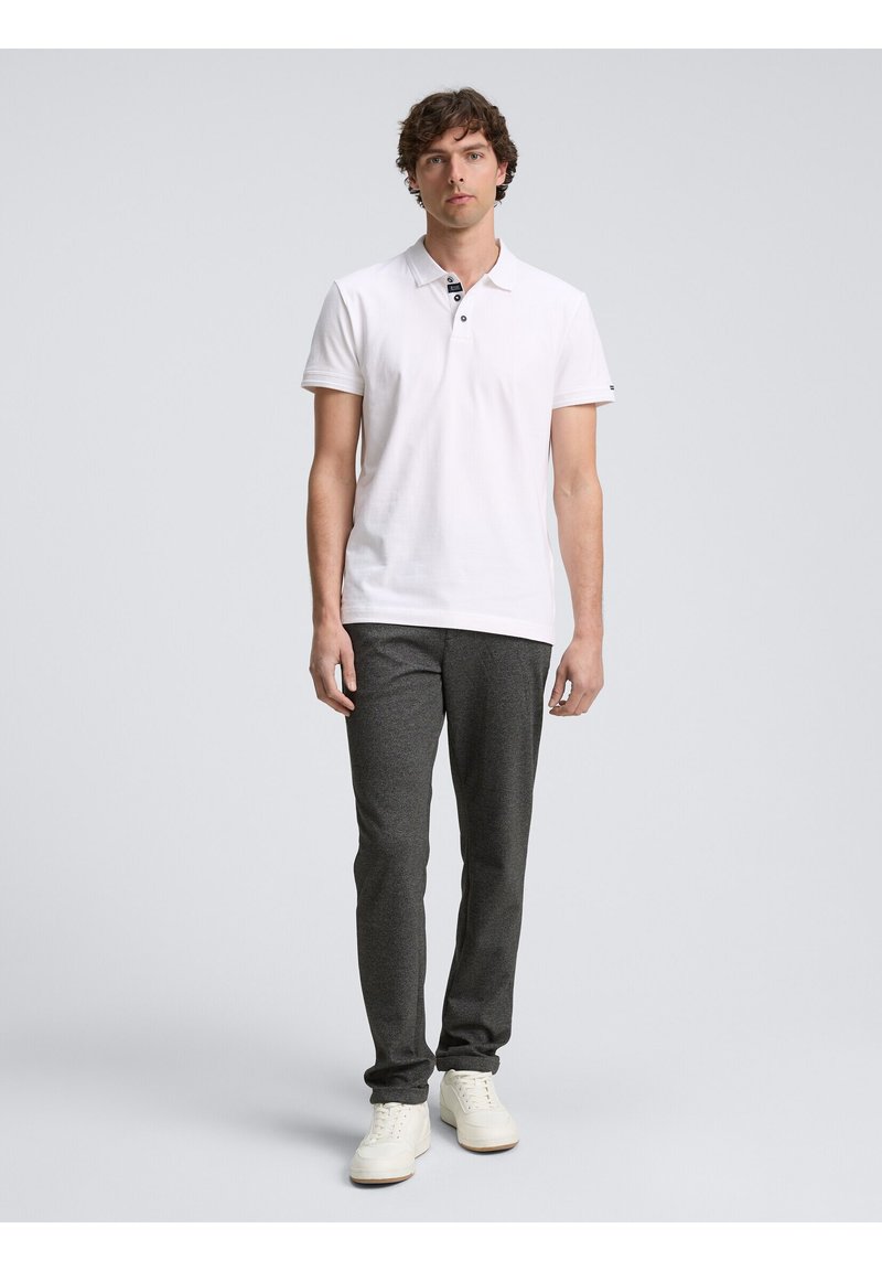 Chemise polo blanche avec un col et deux boutons, associée à un pantalon gris foncé ajusté et des baskets blanches. Design simple et décontracté.