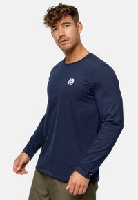Camiseta de manga larga azul marino, confeccionada en tela suave, con cuello redondo y un pequeño logo blanco en el pecho. Diseño sencillo y ajustado.