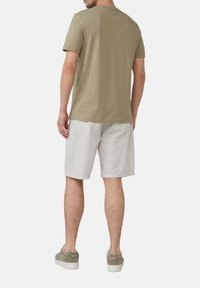 Olijfgroene katoenen T-shirt, korte mouwen, ronde hals; gecombineerd met lichtgrijze mesh shorts en grijs-groene sneakers met witte zolen.