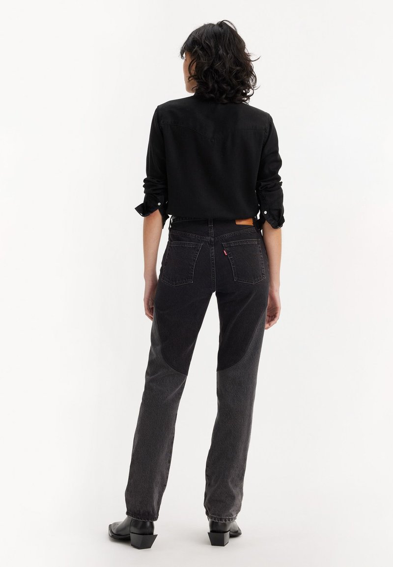 Vaqueros de mezclilla negros con una cintura alta, con un corte ajustado y paneles texturizados en contraste en las piernas. Costura visible en el bolsillo trasero.