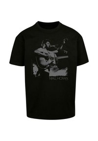 Sort t-shirt med et grafisk motiv af en mandlig figur, der spiller akustisk guitar, med "NIALL HORAN" trykt nedenfor i hvid tekst.