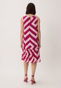 Ärmelloses Kleid in Pink und Creme mit Zickzackmuster, gerafftem Saum und Knopfverschluss auf der Rückseite. Kombiniert mit passenden pinken High Heels.