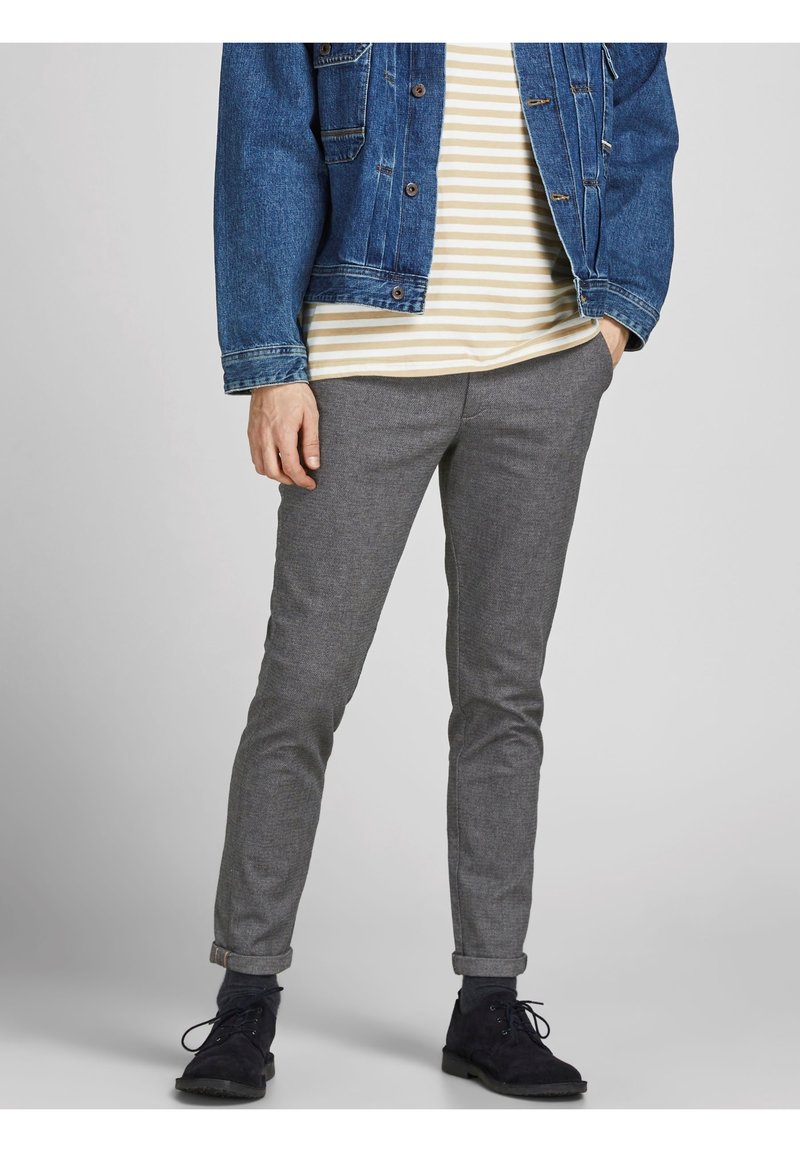 Veste en jean bleue, chemise rayée beige et blanche, pantalon gris fuselé et chaussures en daim noires. Tenue décontractée avec des couleurs contrastées.