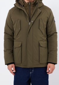 Chaqueta acolchada de color verde oliva con capucha, con cierre frontal de cremallera, dos grandes bolsillos con solapa y una capa interior acolchada.