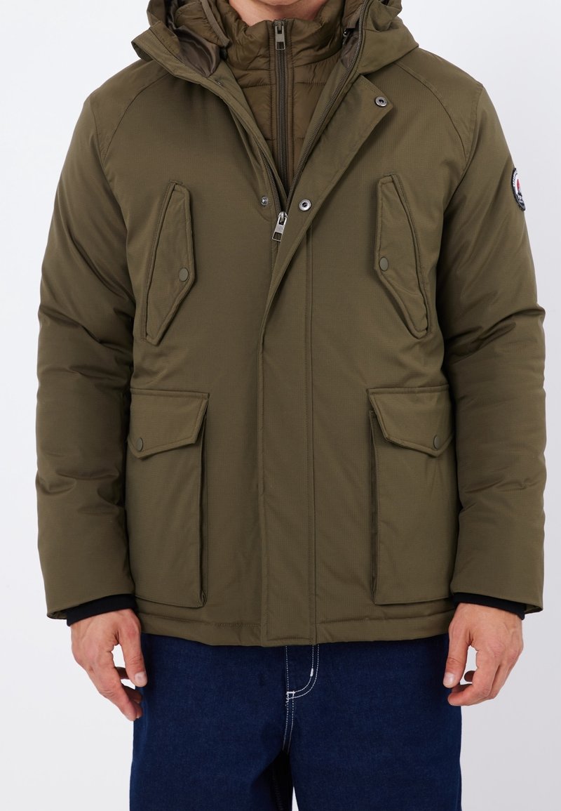 Chaqueta acolchada de color verde oliva con capucha, con cierre frontal de cremallera, dos grandes bolsillos con solapa y una capa interior acolchada.