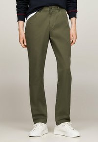 Pantaloni in cotone verde oliva con una vestibilità dritta, dotati di tasche frontali e chiusura con bottone, abbinati a sneakers bianche.