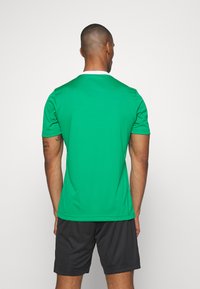 Grønn atletisk skjorte med korte ermer og hvit krage, kombinert med svarte shorts. Glatt stoff med vanlig passform. Ingen synlige mønstre.
