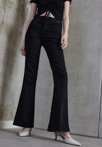 Czarne dżinsy w kształcie dzwonów z wysokim stanem, wykonane z denimu. Połączone z jasnymi butami na obcasie typu slingback. Strukturalny design z detalami szwów.
