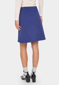 Jupe A-line bleue en tissu doux, avec une texture lisse et une taille élastique. Associée à des chaussures à talons noires et des chaussettes grises.