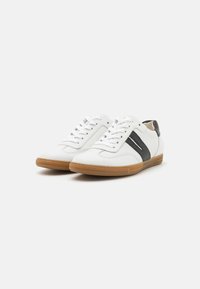 Baskets blanches avec des accents en cuir noir, matériau supérieur texturé et semelle en gomme. Elles disposent de lacets ronds et d'un design minimaliste.