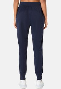 Marineblauwe sportbroek met een tapered fit, elastische tailleband, zijzakken en een gladde, gestructureerde stof, gecombineerd met witte sneakers.