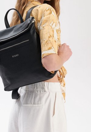 Zwarte leren rugzak met een gestructureerde afwerking, voorzien van een ritssluiting en een voorvak. Het ontwerp omvat verstelbare riemen en zilverkleurige hardware.