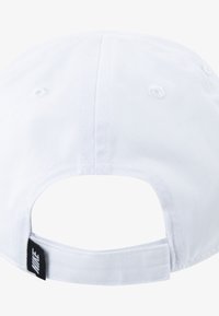 Cappellino da baseball bianco con visiera curva, cinturino posteriore regolabile e una piccola etichetta nera con il logo vicino al cinturino. Il tessuto ha una texture liscia.
