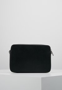 Borsa a tracolla rettangolare nera in pelle con zip argentata, esposta su un piedistallo bianco contro uno sfondo grigio uniforme.