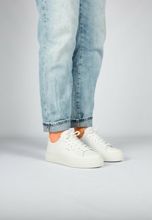 Witte sneakers met een glad leren bovenkant, ronde neus en opvallende veters. Beschikt over een dikke zool, gecombineerd met lichtblauwe opgerolde spijkerbroek.