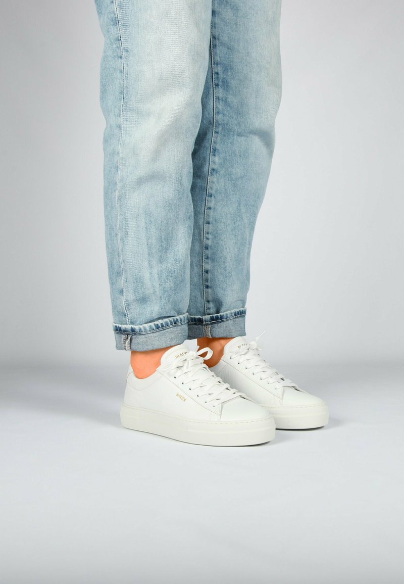 Weiße Sneakers mit einem glatten Lederobermaterial, runder Spitze und auffälligen Schnürsenkeln. Mit dicker Sohle, kombiniert mit hellblauen hochgekrempelten Jeans.
