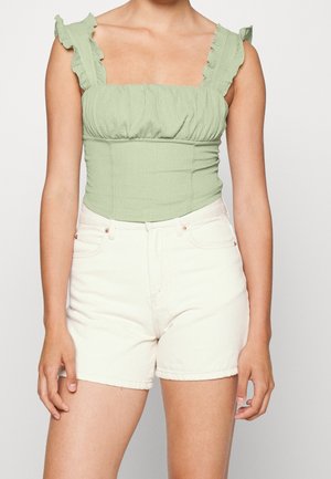Lichtgroene top met smockwerk en gerimpelde bandjes, gecombineerd met witte denim shorts. De top heeft een vierkante hals en een geplooide textuur.
