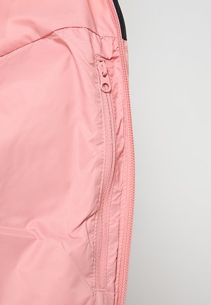 Interno di giacca in tessuto rosa chiaro, liscio, con tasca con cerniera e dettagli di cuciture a contrasto lungo i bordi.