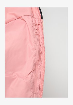 Interno di giacca in tessuto rosa chiaro, liscio, con tasca con cerniera e dettagli di cuciture a contrasto lungo i bordi.