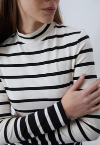 Haut à manches longues rayé avec un col montant, présentant des rayures horizontales noires et blanches alternées, fabriqué dans un tissu doux et extensible.