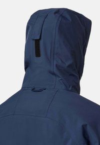 Marinblå vattentät jacka med en strukturerad huva, utrustad med ett kardborretab, slät textur och rena sömmar. Designen betonar minimalism.