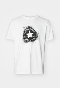 Camiseta blanca de algodón con un gráfico circular negro de "Converse All Star" con una estrella en el centro y acentos de diseño de salpicaduras.