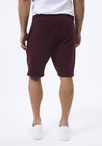 Bordeaux atletiske shorts i et tekstureret stof, knælange med en elastisk waistband, båret med hvide slip-on sko.