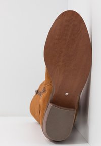 Bottine en daim marron avec une semelle en caoutchouc texturée. Taille 37 indiquée en dessous, équipée d'une fermeture éclair latérale et d'accents lisses.