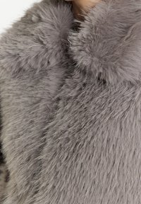 Manteau en fausse fourrure grise avec une surface douce et texturée et un col en peluche. Présente un design volumineux avec de longues fibres sur toute sa longueur.