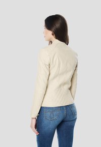 Crèmekleurig leren jack met een aansluitend ontwerp, doorgestikte details op de schouders en lange mouwen. Gecombineerd met blauwe spijkerbroek.