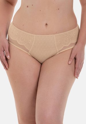 Beige lace women's underwear with floral and diamond patterns worn by a person with hands resting on their thighs against a white background.