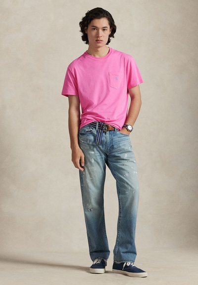 Ροζ βαμβακερό μπλουζάκι με μικρή τσέπη, τζιν παντελόνι σε μπλε αποχρώσεις με σημεία βαφής, και ναυτικά αθλητικά παπούτσια, ολοκληρωμένα με ριγωτή ζώνη.