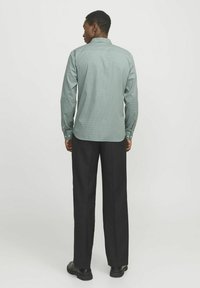 Camicia verde a fantasia con colletto button-down, abbinata a pantaloni neri. La camicia presenta una texture opaca e un design aderente.