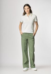 Polo shirt bianco con bordi gialli e verdi, abbinato a pantaloni larghi verdi. Sneakers bianche completano l'outfit.