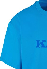 Blue cotton t-shirt with short sleeves, round neckline, and a glossy blue logo print on the front. Smooth texture and standard fit.
