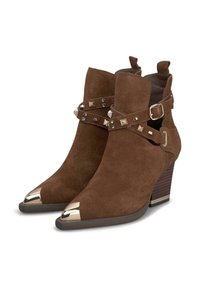 Botas de tobillo de ante marrón con punteras puntiagudas, acentos de chapa metálica plateada y hebillas decorativas con detalles de tachuelas. Tacón bajo apilado.