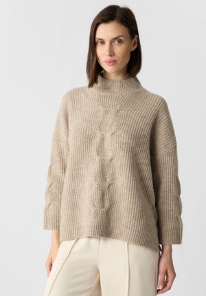 Beige Strickpullover mit hohem Kragen, geripptem Textur und weiten Ärmeln, versehen mit einem zentralen Kabelmuster und einer lockeren Passform.