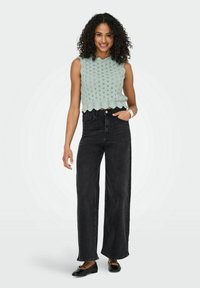 Muntgroene gebreide cropped top met golvende randen, gecombineerd met hoge zwarte wijde jeans en zwarte platte schoenen.
