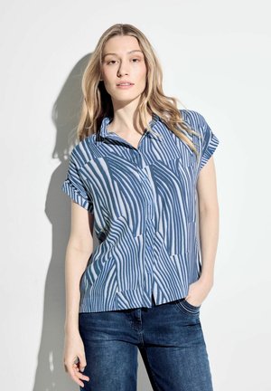 Kurzarmpoloshirt im Blau-weiß gestreiften Muster, mit Kragen und lockerer Passform, kombiniert mit dunklen Jeans.