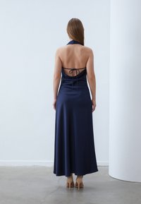 Mornarska saten halter maksi haljina s otvorenim leđima, vezana detaljima, lepršavim siluetom i glatkom teksturom. Ima elegantan, minimalistički dizajn.